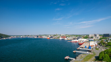 Naklejka na ściany i meble St. John's, Newfoundland, Canada - September 2021: Harbor view of the downtown area of St. John's with large offshore oil supply vessels and salmon farming feed transport boats tied to the dock. 
