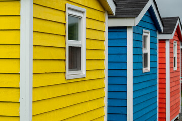 The exterior of a bright yellow and blue wooden clapboard wall of a shed house with one vinyl window. The trim on the glass panes is white in color. The outside boards are textured pine wood. 