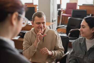 Two girls and a guy are talking in sign language. Three deaf students chatting in a university classroom. © Михаил Решетников