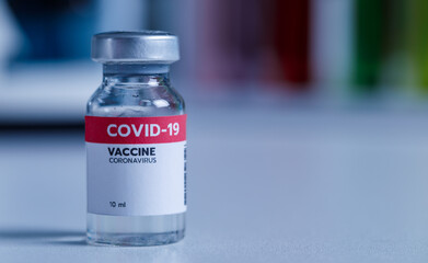 Close up shot of 10 ml coronavirus covid 19 vaccine in small glass vial bottle with red label for protection prevention epidemic pandemic virus outbreak around world in laboratory blurred background