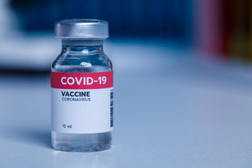 Close up shot of 10 ml coronavirus covid 19 vaccine in small glass vial bottle with red label for protection prevention epidemic pandemic virus outbreak around world in laboratory blurred background