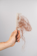 Close-up of a female hand holding a comb with a bun of hair on a white background. Hair loss and...