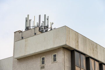 Panel antennas of a mobility cell site on the roof of a concrete building against a blue sky
