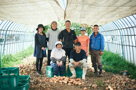 収穫した玉ねぎの前で微笑む3世代農家とベトナム研修生