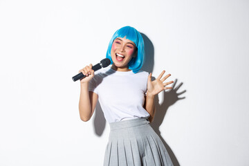 Cheerful cute asian girl dressed up as anime character for halloween party, wearing blue wig and...