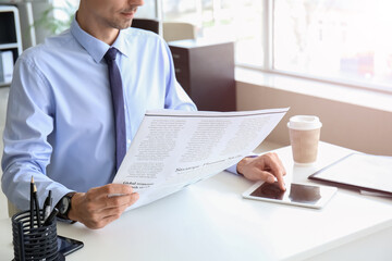 Young businessman reading newspaper while using tablet computer in office