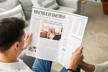 Young man reading newspaper at home - obrazy, fototapety, plakaty