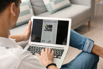 Young man reading newspaper online at home