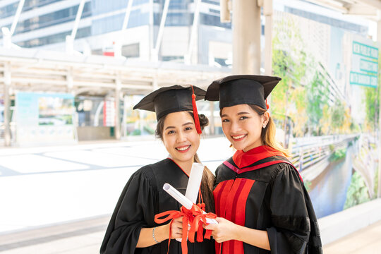 Two Asian women wore graduate gowns are looking forward to the camera and smiling widely