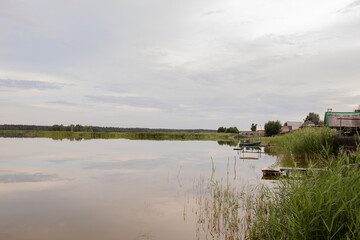 The mirror-like surface of the lake on the outskirts of the village with old piers and boats. Cloudy weather, evening.