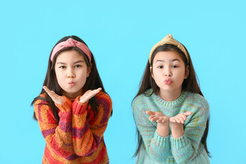 Cute little sisters blowing cheeks on color background