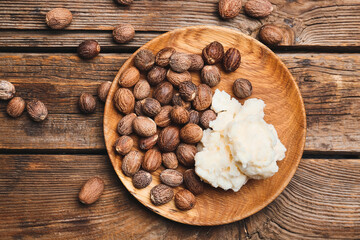 Fototapeta na wymiar Plate with shea butter and nuts on wooden background
