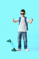 Little schoolboy with skateboard showing thumbs-up on color background