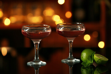 Glasses of tasty cosmopolitan cocktail and lime on table in bar