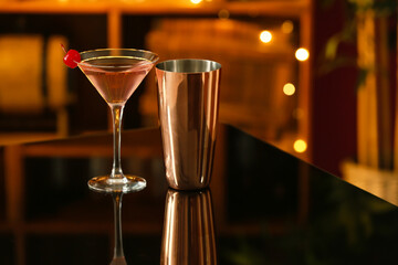 Glass of tasty cosmopolitan cocktail and shaker on table in bar