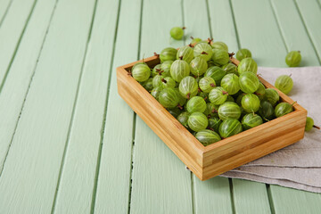 Box with fresh ripe gooseberry on color wooden background