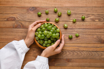 Woman with fresh ripe gooseberry on wooden background