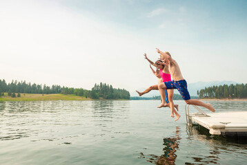 Group of kids jumping off the dock into the lake together during a fun summer vacation. 