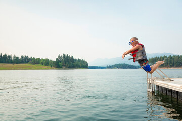 Cute little daring boy jumping off the boat dock at the lake. Being adventurous and brave, diving...