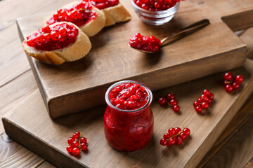 Jar of red currant jam and sandwiches on wooden background, closeup