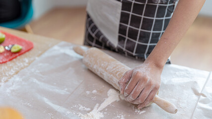 Young attractive Asian girl takes wood roller or thresher to make bread in her kitchen for lunch on a holiday
