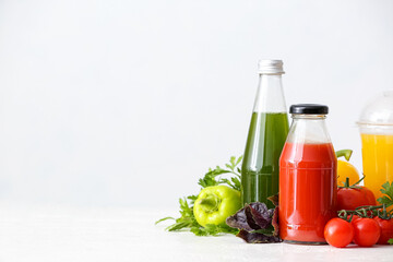 Bottles with healthy juice, fruits and vegetables on light background