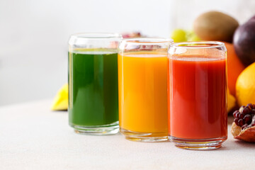 Glasses with healthy juice, fruits and vegetables on light background