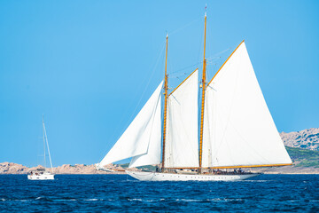 Fototapeta premium Stunning view of a wooden sailboat with white sails sailing on a blue water during a sunny day. Isola di Spargi, Maddalena Archipelago,Sardinia, Italy.