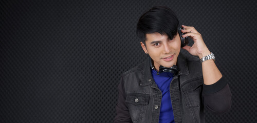 Young asian DJ listen to  headphones while his mixes are playing. Musician producing music in professional recording studio.