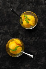 Mango yellow ice cream with fruits and mint in glass bowls with spoons. Top view, on the dark table