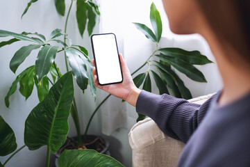 Mockup image of a woman holding mobile phone with blank desktop screen at home