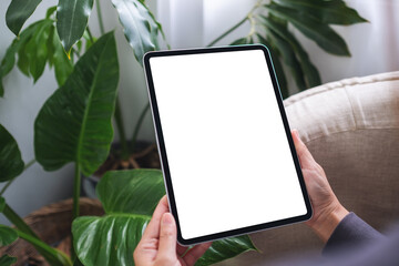 Mockup image of a woman holding digital tablet with blank white desktop screen at home