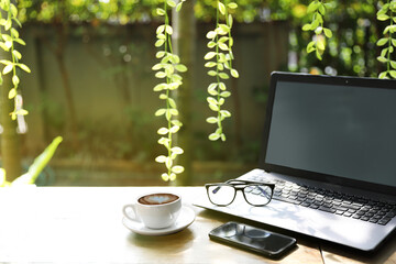 Wooden table  with smart phon, cup of coffee and lap top of work space outdoor, concept relax with garden and sunlight background - image