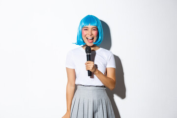 Image of beautiful japanese girl in blue anime wig, singing karaoke in microphone, smiling happy,...
