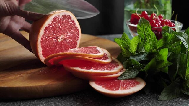 Knife slicing orange red citrus fruit grapefruit on a wooden board for making summer refreshing drink - lemonade