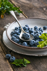 Freshly picked blueberries in a  bowl. Juicy and fresh berries with green leaves on a rustic table.  Healthy food and nutrition concept