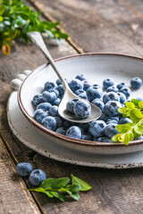 Freshly picked blueberries in a  bowl. Juicy and fresh berries with green leaves on a rustic table.  Healthy food and nutrition concept