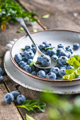 Freshly picked blueberries in a  bowl. Juicy and fresh berries with green leaves on a rustic table.  Healthy food and nutrition concept