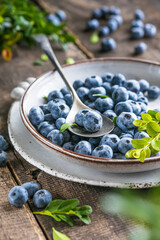 Freshly picked blueberries in a  bowl. Juicy and fresh berries with green leaves on a rustic table.  Healthy food and nutrition concept
