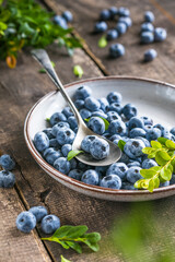 Freshly picked blueberries in a  bowl. Juicy and fresh berries with green leaves on a rustic table.  Healthy food and nutrition concept