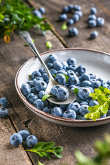 Freshly picked blueberries in a  bowl. Juicy and fresh berries with green leaves on a rustic table.  Healthy food and nutrition concept