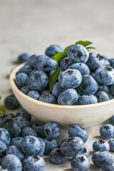 Freshly picked blueberries in a  bowl. Juicy and fresh berries with green leaves on a rustic table.  Healthy food and nutrition concept