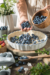Woman putting blueberrie  into baking dish to make traditional English pie, closeup