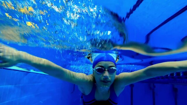 Under water view of professional female swimmer . Underwater footage of woman jumping into water . Swimmer jumping in big swimming large pool. Woman swimmer dive in water pool .  Slow Motion .