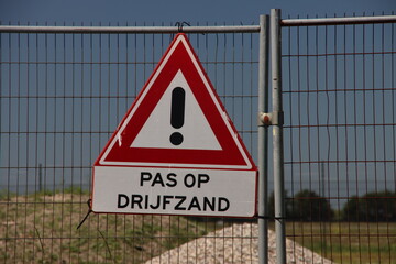 Warning sign for quicksand at construction site on fence - obrazy, fototapety, plakaty