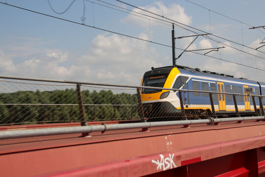 SNG regional commuter with yellow front runs over the Hanzeboog red steel bridge over River IJssel nearby Zwolle