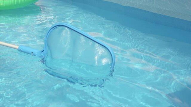 SLOW MOTION, CLOSE UP: Unrecognizable pool cleaner uses a leaf net during maintenance works. Plastic pool skimmer cleans up tiny leaves from the glassy pool water. Person cleaning pool in the backyard