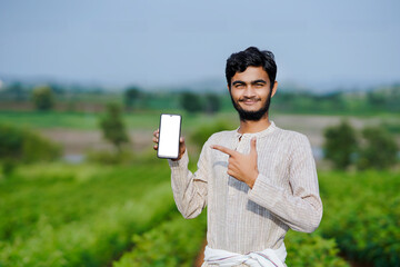 Indian farmer Showing a mobile screen at green cotton crop