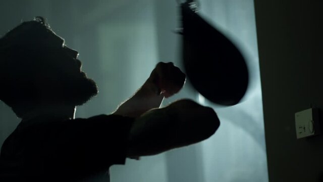 Young professional boxer boxing speed punching bag . Side view of young boxer practicing hand speed drill in slow motion using small punching bag in boxing gym .  Sportsman boxing in smoky studio .