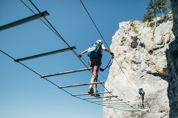 Climber on via ferrata  crossing suspended wire bridge